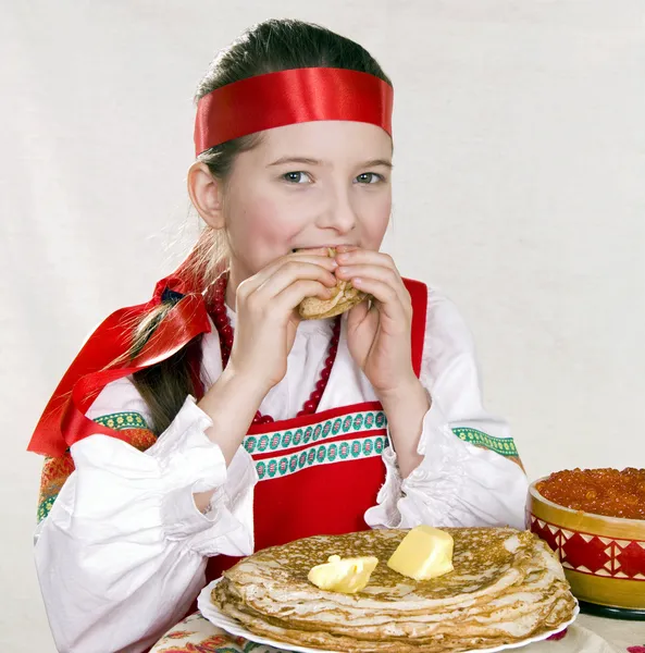 俄罗斯姑娘后面吃煎饼的表 免版税图库照片
