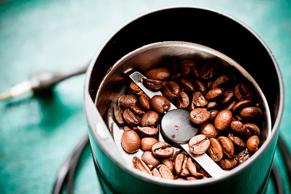 Máquina eléctrica de molino de café con granos de café tostados en la mesa verde —  Fotos de Stock
