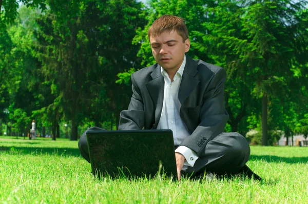 Geschäftsmann in einem Park auf dem Rasen workin auf Laptop — Stockfoto