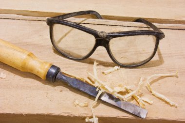 Protective glasses and chisel on wood table clipart