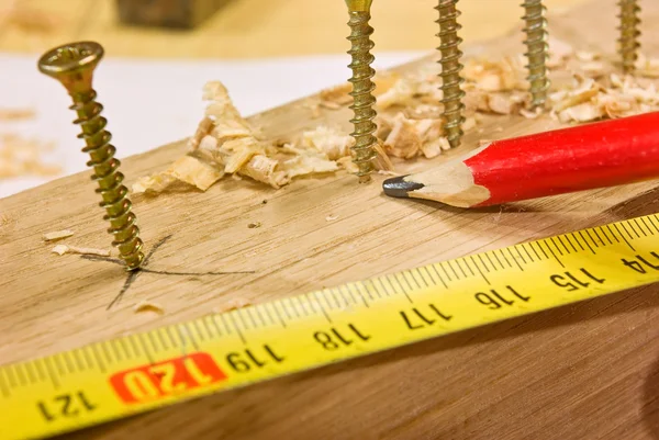 Винты, карандаш и лента для измерения на деревянной доске — стоковое фото